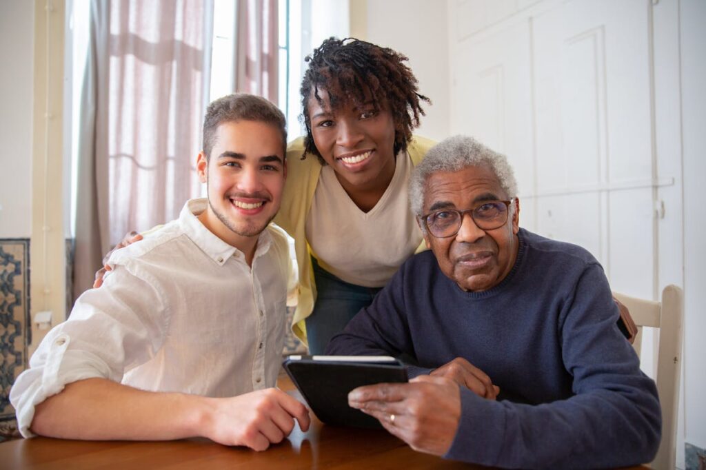 pexels-photo-7551617 Elderly man enjoying technology with diverse caregivers at home.